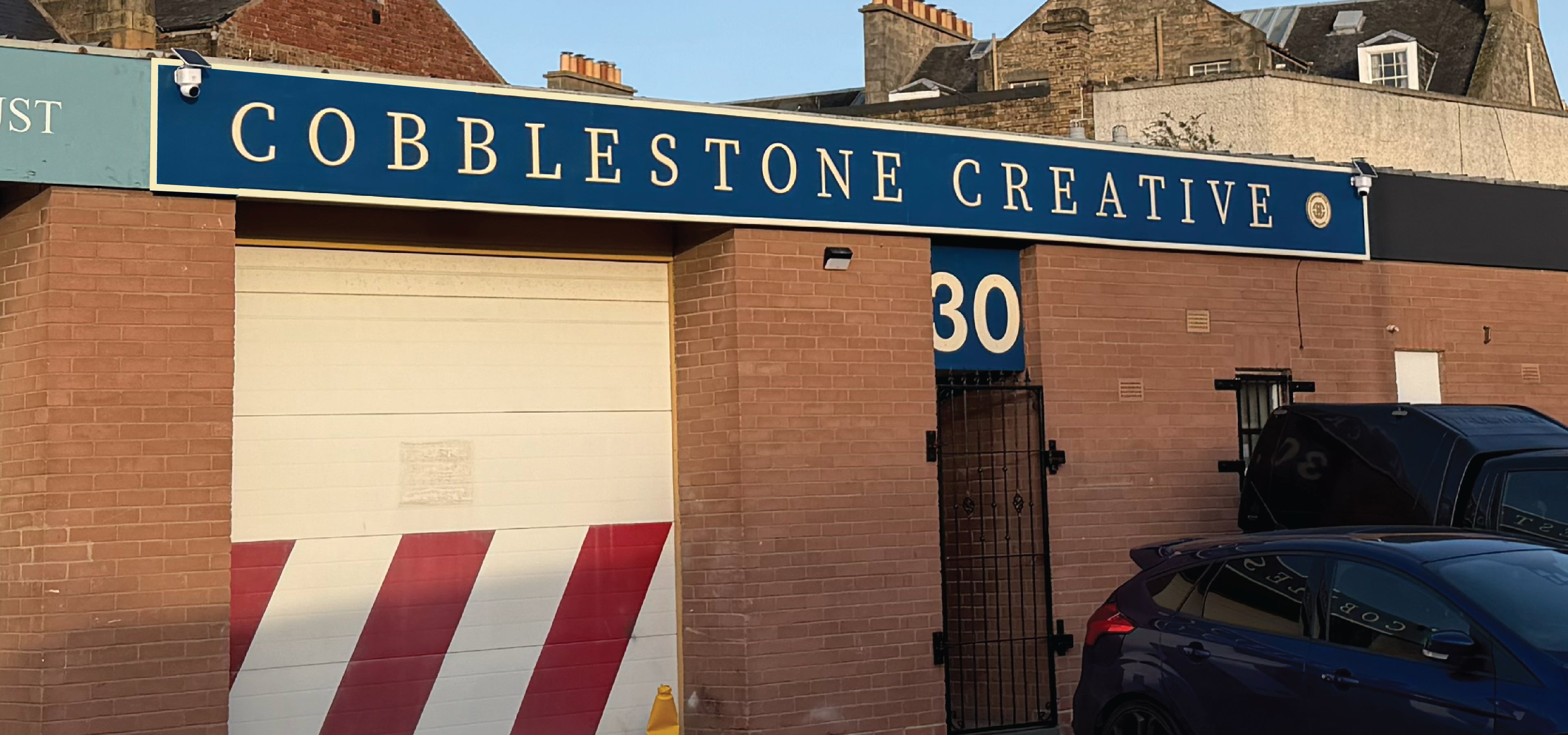 Cobblestone Creative sign on a brick building with cars parked below.