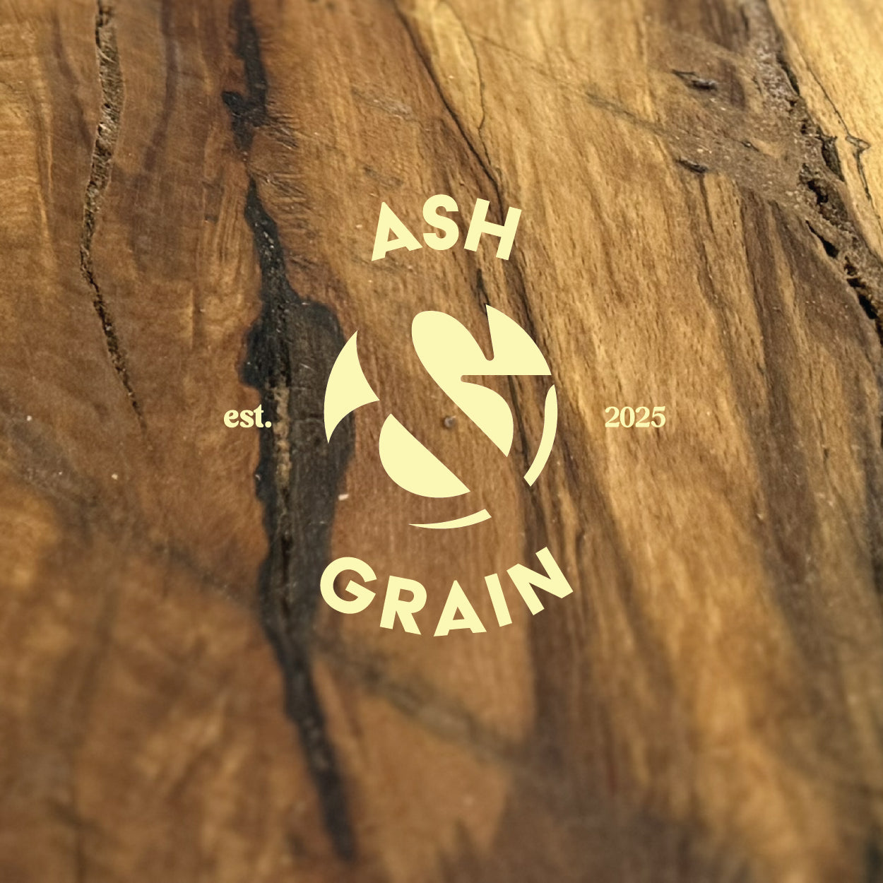 Ash & Grain logo overlaid on the grain of a hardwood slab.