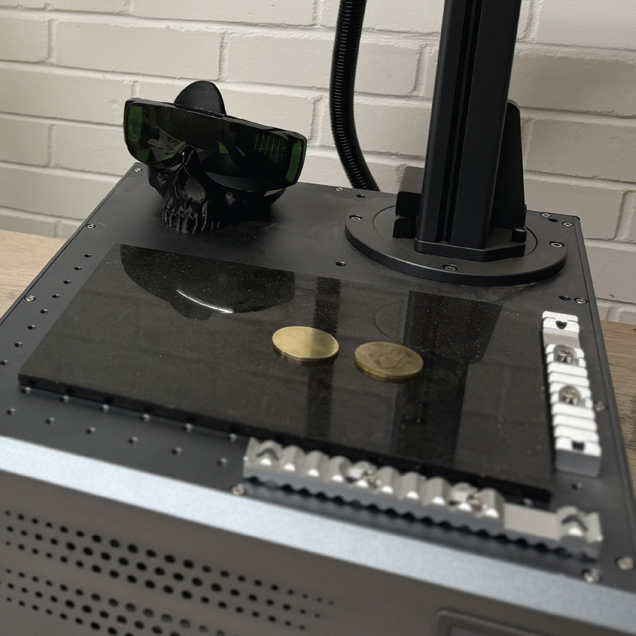 Brass coins on the work area of a 100W Fibre MOPA laser at Cobblestone Creative workshop.